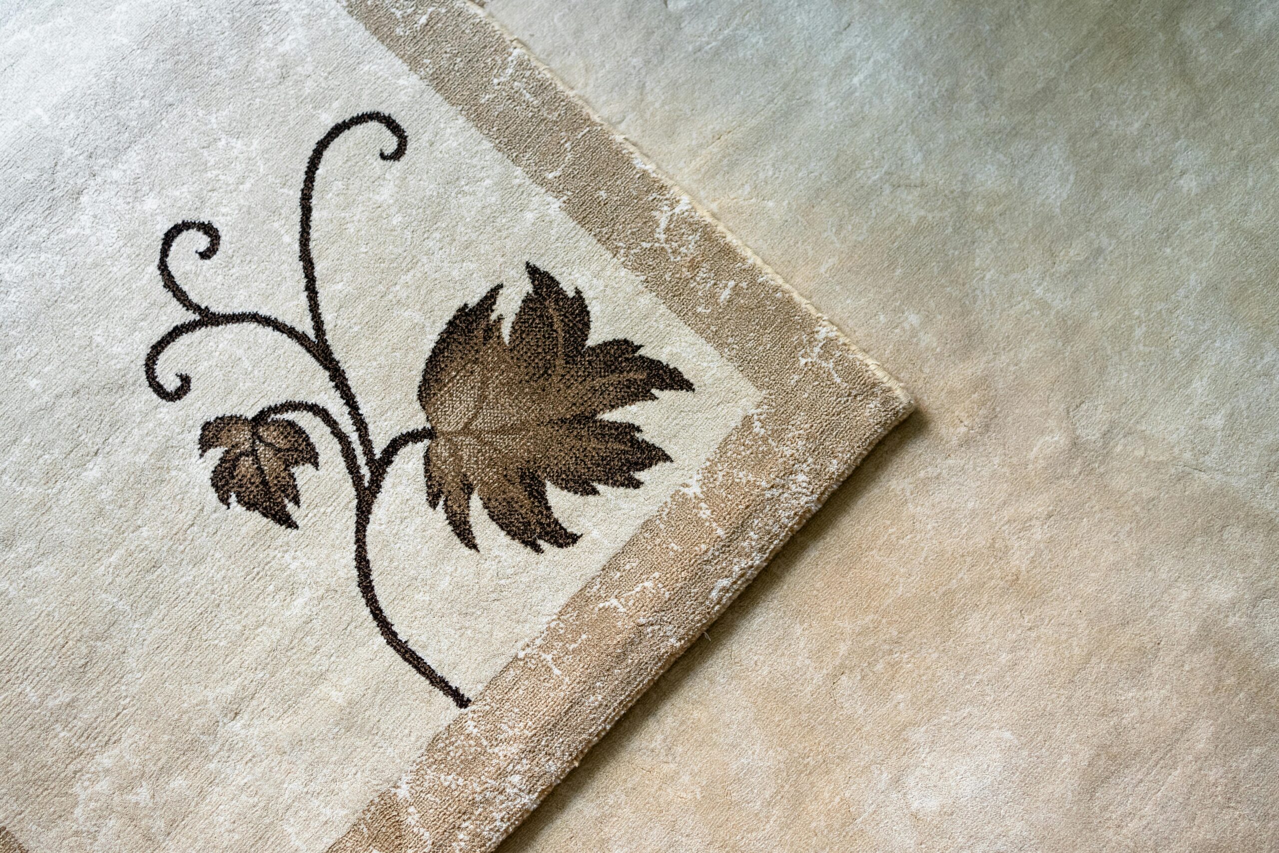 How To Choose The Perfect Rug For Your Living Room A close-up of a beige carpet with an elegant leaf design, showcasing intricate detail and texture.