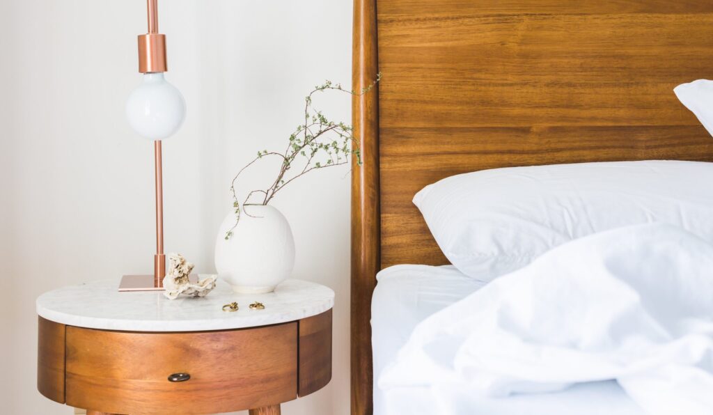 A modern bedroom setup featuring a wooden bed, stylish lamp, and round side table with a plant.
