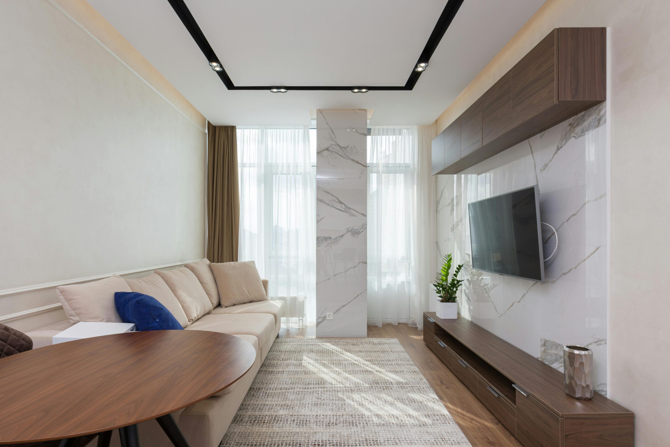 How To Choose The Perfect Rug For Your Living Room Comfortable sofa with soft cushions and round wooden table placed in front of modern TV set hanging on wall in cozy living room