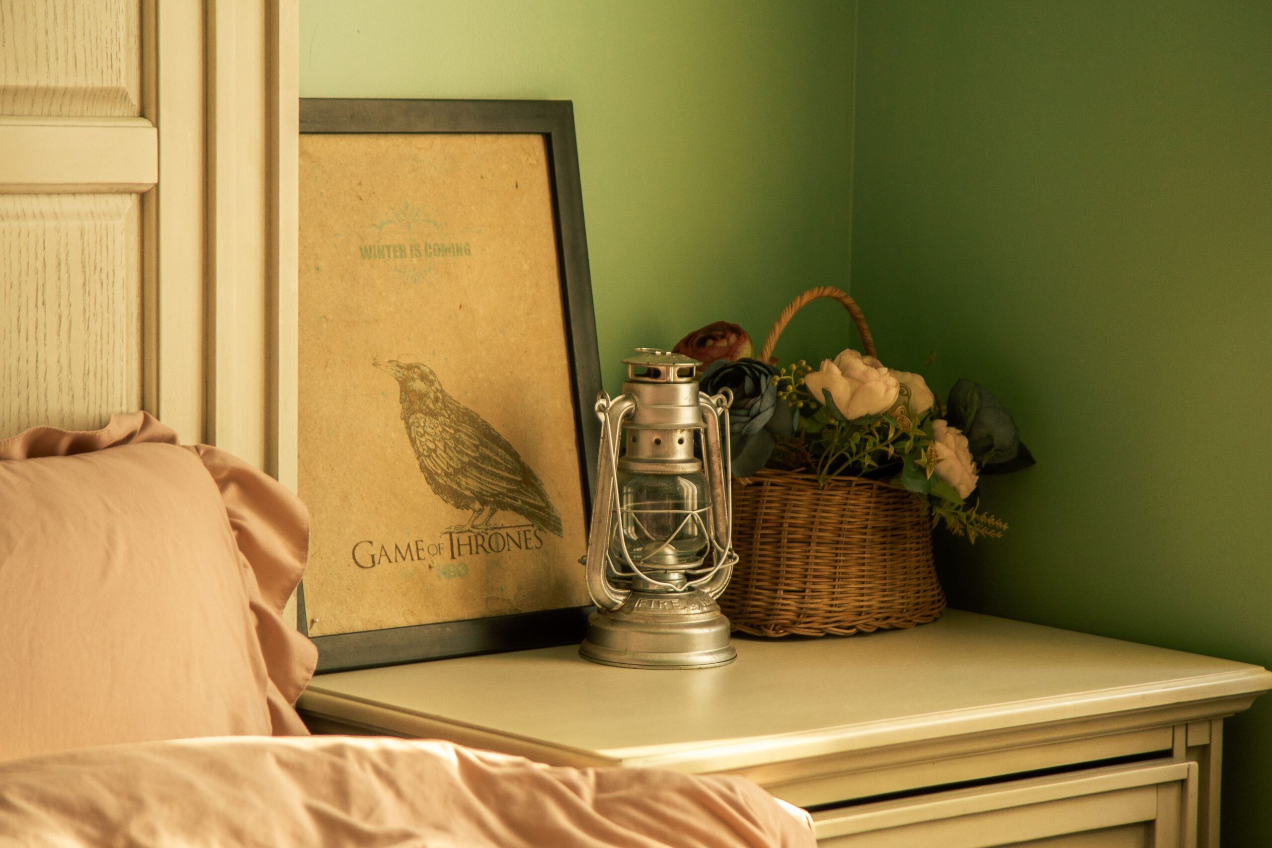 How To Choose The Perfect Nightstands For Your Bedroom Warmly lit bedroom corner with poster, lantern, and floral basket adding vintage charm.