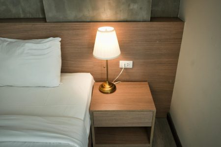 How To Choose The Perfect Nightstands For Your Bedroom Elegant bedroom setup with a lamp on a wooden nightstand, creating a cozy ambiance.