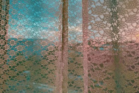 How To Choose The Perfect Curtains For Your Space White lace curtain hanging on window with view of modern residential complex houses in early evening