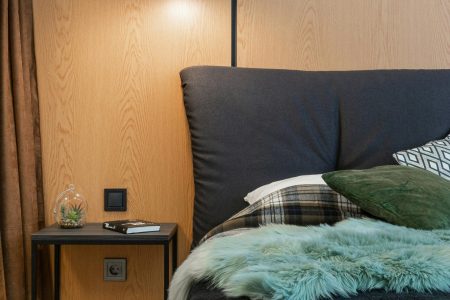 How To Choose The Perfect Nightstands For Your Bedroom Comfortable bed with pillows and soft blanket placed at wooden wall near bedside table in modern light bedroom at home