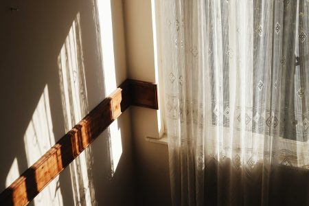 How To Choose The Perfect Curtains For Your Space Tranquil scene of sunlight casting soft shadows through a lace curtain in a cozy room corner.